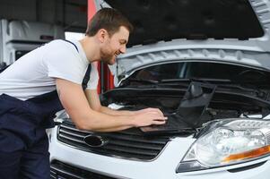 Auto Mechaniker mit ein Computer Laptop zu Diagnose und Überprüfung oben auf Auto Motoren Teile zum Festsetzung und Reparatur foto