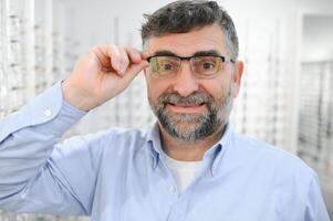 Brille überprüfen, Senior Vision und Alten Mann beim ein Beratung Optometrie Klinik zum Wohlbefinden. Glücklich, Lächeln und alt Gesicht mit Linse, Rahmen und Brillen Wahl im ein Geschäft zum Hilfe bekommen ein Verschreibung. foto