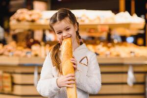 wenig Mädchen mit ein Stangenbrot im das Geschäft foto