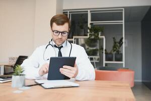 männlich Arzt mit Tablette Computer beim seine Büro. Allgemeines Praktiker mit Digital Tablette beim seine Klinik. foto