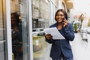 ein ziemlich afrikanisch amerikanisch Geschäft Frau reden auf ein Zelle Telefon beim Büro Gebäude foto