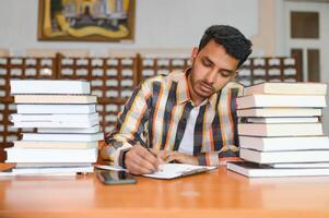 Porträt von heiter männlich International indisch Schüler mit Rucksack, Lernen Zubehör Stehen in der Nähe von Bücherregale beim Universität Bibliothek oder Buch Geschäft während brechen zwischen Unterricht. Bildung Konzept foto