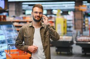 glücklich Mann Kauf gesund Essen und trinken im ein modern Supermarkt und reden auf Telefon. foto