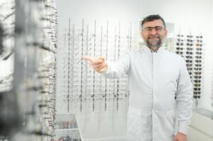 Porträt von ein gut aussehend Augenarzt im Vorderseite von das Vitrine mit Brille im das Krankenhaus. foto