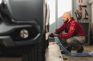 Auto Mechaniker Schrauben oder abschrauben Auto Rad von angehoben Automobil durch pneumatisch Schlüssel beim Reparatur Bedienung Bahnhof foto