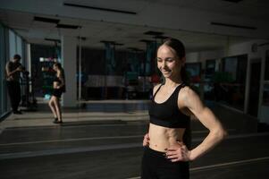 Brünette sexy Fitness-Mädchen in Sportbekleidung mit perfektem Körper im Fitnessstudio posiert vor dem Trainingsset foto
