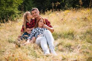 Familie von drei Menschen sich ausruhen im das Berge. Sie saß Nieder zu ausruhen, trinken Wasser nach ein schwer steigen zu das Berg. Sie sind müde aber glücklich foto