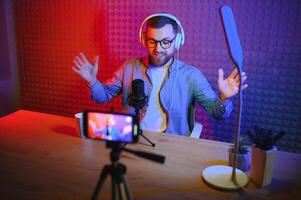 vlogger mit Smartphone zu Film Podcast im Studio. Blogger mit Handy, Mobiltelefon Telefon, Mikrofon und Kopfhörer filmen Video zum Sozial Medien Rundfunk- Karriere. foto