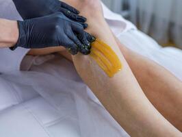 Frau Kosmetikerin führt aus Zuckern Peeling auf ihr Beine foto
