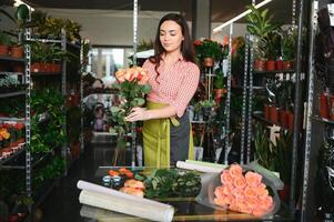 süß Mädchen Florist sammelt ein Strauß von Rosen im ein Blume Geschäft. ein schön Florist schafft ein Komposition von Blumen. Mädchen schneidet Blumen und entfernt abgestanden Blätter foto