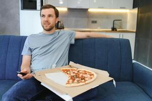 isst Pizza während Aufpassen Fernseher zeigen. Mann mit Bart drinnen. foto