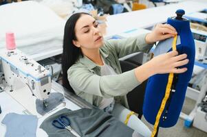 jung Schneider Frau näht Kleider auf Arbeiten Tisch. lächelnd Näherin und ihr Hand schließen oben im Werkstatt. foto