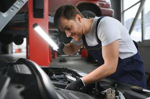 ein Mechaniker ist tun Auto Untersuchung unter das Kapuze mit Taschenlampe beim Mechanik Geschäft. foto