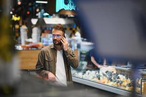 glücklich Mann Kauf gesund Essen und trinken im ein modern Supermarkt und reden auf Telefon. foto