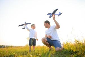 Papa mit seine Sohn beim Sonnenuntergang im Natur. ein Vater Theaterstücke mit Spielzeug Flugzeuge mit seine Sohn beim Sonnenuntergang. Vaters Tag foto