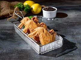 knusprig Hähnchen Flügel im tief Friteuse mit Limette und schwarz Pfeffer oben Aussicht auf dunkel Hintergrund foto