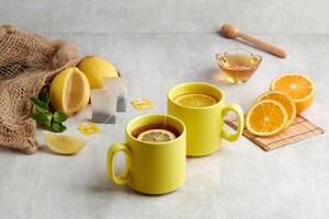 zwei Gelb Tasse von Erwärmen Honig Zitrone Tee mit Scheiben von Orange und Zitrone. foto