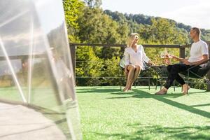 glücklich Paar sitzen auf Korbweide Stühle beim draussen Terrasse im das Berge und trinken Wein. romantisch Zeit zusammen. foto