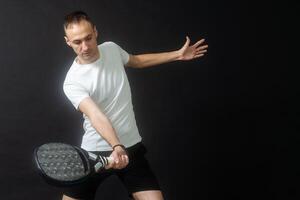 Porträt von Mann spielen Paddel Tennis im Position zu schlagen ein Rückhand Ball schwarz isoliert Hintergrund. Vorderseite Sicht. foto