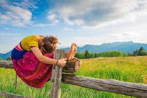 lässiges Mädchen entspannt sich beim Dehnen und Yoga allein in den Bergen über einem Zaun in einer schönen Frühlingswiese.