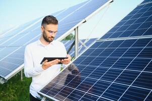 das Porträt von ein jung Ingenieur prüft mit Tablette Betrieb mit Sonne, Sauberkeit auf Feld von Photovoltaik Solar- Tafeln. Konzept verlängerbar Energie, Technologie, Elektrizität, Service, Grün Leistung. foto