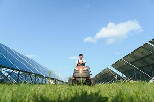 ein Mann Arbeiten beim Solar- Leistung Bahnhof. ein Arbeiter auf ein Garten Traktor mäht Gras auf ein Solar- Panel Bauernhof. foto