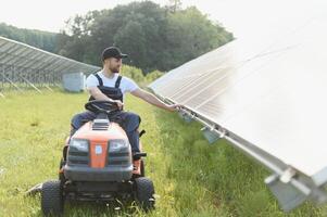 ein Mann fährt ein Rasenmäher in der Nähe von Solar- Tafeln. Konzept von Solar- Energie foto