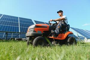 ein Mann mäht das Gras in der Nähe von das Solar- Tafeln. Grün Energie foto