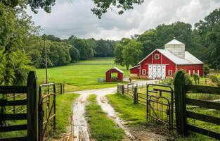 ai generiert rot Scheune und rot Scheune Haus im üppig Grün Feld mit Schmutz Straße und hölzern Zaun im das Vordergrund. foto