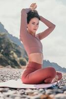 Mitte alt Gut suchen Frau mit schwarz Haar, Fitness Lehrer im Gamaschen und Spitzen tun Dehnen und Pilates auf Yoga Matte in der Nähe von das Meer. weiblich Fitness Yoga Routine Konzept. gesund Lebensstil foto