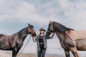 jung glücklich Frau im Hut mit ihr Pferd im Abend Sonnenuntergang Licht. draussen Fotografie mit Mode Modell- Mädchen. Lebensstil Stimmung. Konzept von draussen Reiten, Sport und Erholung. foto