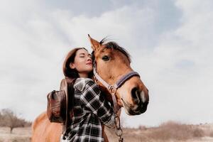 jung glücklich Frau im Hut mit ihr Pferd im Abend Sonnenuntergang Licht. draussen Fotografie mit Mode Modell- Mädchen. Lebensstil Stimmung. Konzept von draussen Reiten, Sport und Erholung. foto