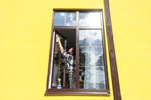 ein Frau manuell wäscht das Fenster von das Haus mit ein Lappen mit ein sprühen Reiniger und ein Mopp außen. Sicherheit beim Höhe, Wiederherstellen bestellen und Sauberkeit im das Frühling, Reinigung Bedienung foto