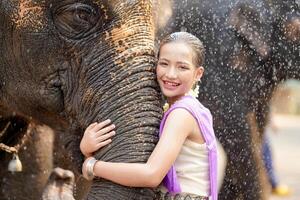 schön ländlich thailändisch Mädchen tragen thailändisch Nord traditionell Kleid Umarmung Kofferraum von asiatisch Elefant mit verschwommen von Wasser sprühen und irgendein Elefant Hintergrund. foto