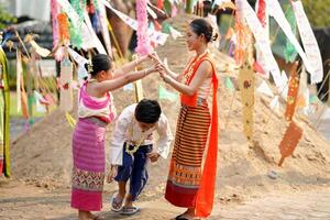 schön thailändisch jung Frauen und Mädchen und Ware thailändisch traditionell Kleid spielen Mensch Höhle Zug mit ein Junge auf Stapel von Sand im Tempel beim das Songkran Festival. foto