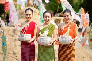 Porträt von schön ländlich thailändisch Frau tragen thailändisch traditionell Kleid Schauspielkunst und halt ein Silber Jahrgang Schüssel zum Foto schießen auf Stapel von Sand im Tempel beim das Songkran Festival.