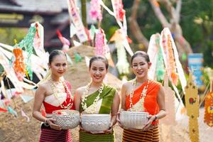 Porträt von schön ländlich thailändisch Frau tragen thailändisch traditionell Kleid Schauspielkunst und halt ein Silber Jahrgang Schüssel zum Foto schießen auf Stapel von Sand im Tempel beim das Songkran Festival.