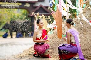 schön thailändisch jung Dame Ware thailändisch traditionell Kleid sitzen chatten und Neckerei jeder andere auf Stapel von Sand im Tempel und verschwommen Hintergrund. foto