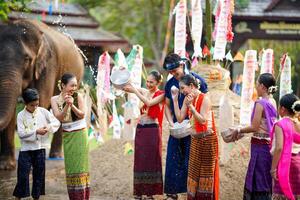 Gruppe von thailändisch Frauen und Kinder Ware thailändisch traditionell Kleid abspielen zu planschen Wasser auf das thailändisch Neu Jahre Tag oder Songkran Festival im ein Spaß Weg auf Elefant und Stapel von Sand Hintergrund. foto