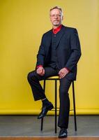 Inhalt Senior Geschäft Mann lächelnd im ein dunkel Anzug. Handson Beine . rot Shirt. zuversichtlich. Geschäft Stil Konzept foto