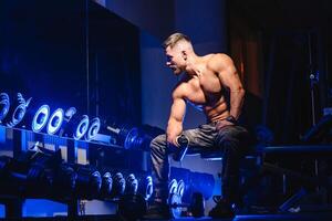 gut aussehend Mann mit groß Muskeln, posieren beim das Kamera im das Fitnessstudio. schwarz und Blau Hintergrund. Porträt von ein Bodybuilder. Nahaufnahme. foto