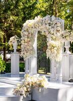 Hochzeit Bogen im das Garten. Weiß Bogen dekoriert mit zärtlich Licht Blumen. foto