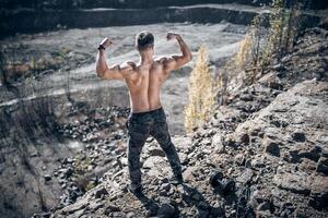 Bodybuilder posieren draussen. Mann Stehen zurück mit angespannt Muskeln. Aussicht von das zurück. Natur Landschaft. foto