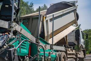 schmeichelhaft Neu Asphalt beim Straße. selektiv Fokus auf Besondere Maschinen. Arbeitskräfte auf verschwommen Hintergrund. foto