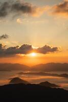 das Sonne ist Rahmen Über ein Berg Bereich, Gießen ein warm glühen Über das Landschaft. das Himmel ist gefüllt mit Wolken, Erstellen ein Sinn von Tiefe und Atmosphäre. das Berge sind bedeckt im ein Nebel foto