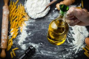 Hand halten Olive Öl Über Vorbereitung brot, Pasta, Pizza Hintergrund. oben Aussicht foto