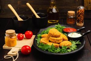 Hähnchen Nuggets auf ein Rucola und Soße, Gewürze, olio auf ein hölzern Hintergrund foto