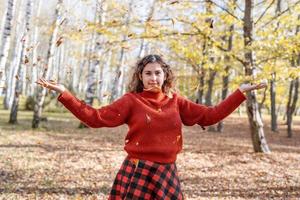 junge glückliche Frau, die Blätter im Herbstwald wirft foto