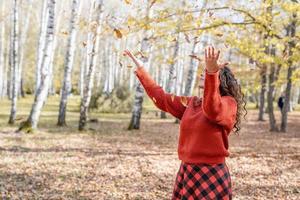 junge glückliche Frau, die Blätter im Herbstwald wirft foto