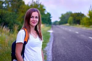 jung Reisen heiter Mädchen steht warten durch das Asphalt Straße mit Bäume foto